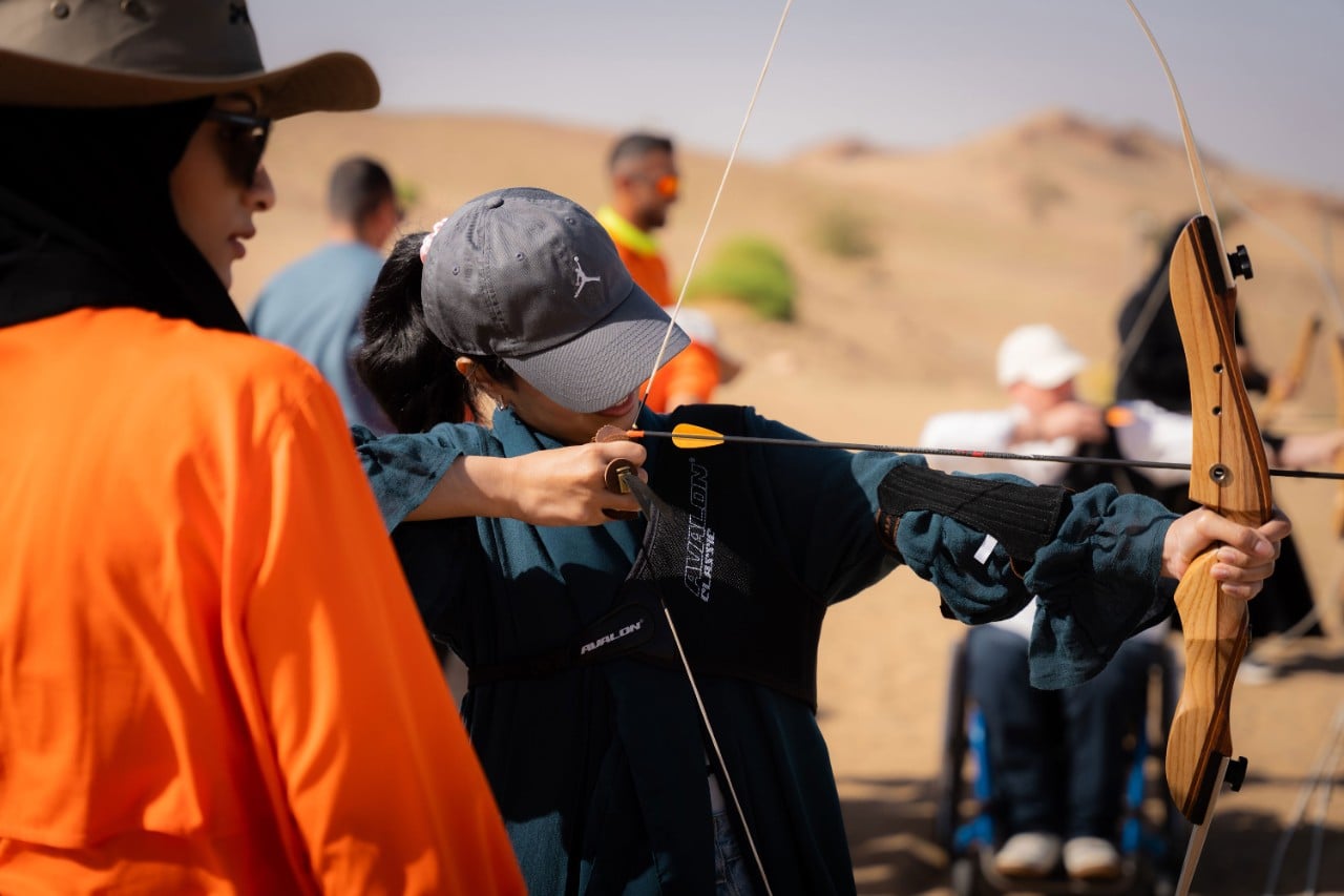 Raneem trying archery at Six Senses Southern Dunes with support from the Akun team, guided by vocal instructions toward the shooting range